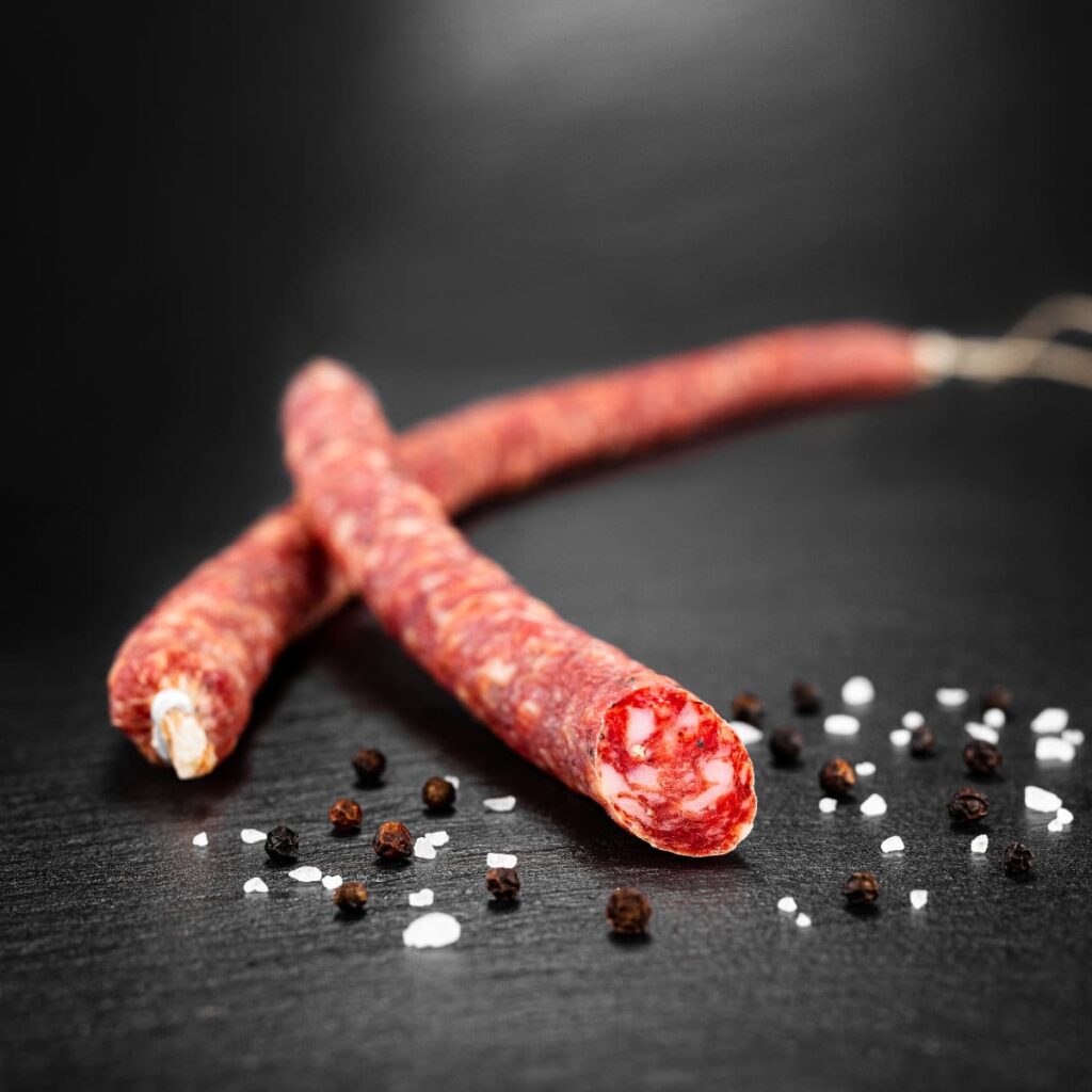 Luftgetrocknete Partywurst in Peitschenform, rustikal angerichtet auf dunklem Untergrund.